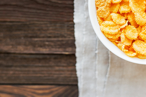 Tasty corn flakes in bowl on homespun napkin. Rustic wooden background. Healthy crispy breakfast snack. Place for text. Top view, flat lay.