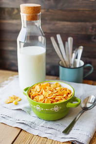 Tasty corn flakes in green bowl with bottle of milk. Rustic wooden background with homespun napkin. Healthy crispy breakfast snack.
