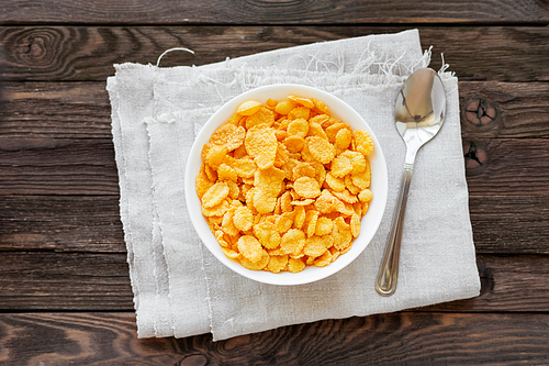 Tasty corn flakes in bowl. Rustic wooden background with homespun napkin. Healthy crispy breakfast snack. Top view, flat lay.