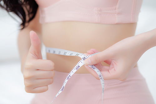 closeup beautiful young asian woman  body slim measuring abdomen for control weight loss in the room, beauty girl belly thin have cellulite with tape measure for diet, health and wellness concept.