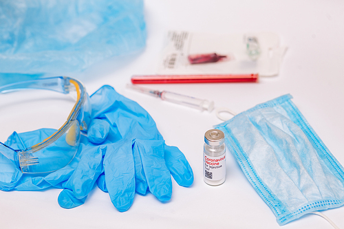 Coronavirus vaccine. Medical preparation in ampoule. Treatment for the disease, covid-19. The vaccine on a white background and on the background of a syringe, rubber gloves and goggles.