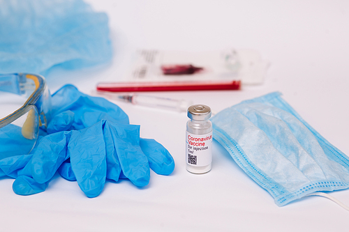 Coronavirus vaccine. Medical preparation in ampoule. Treatment for the disease, covid-19. The vaccine on a white background and on the background of a syringe, rubber gloves and goggles.