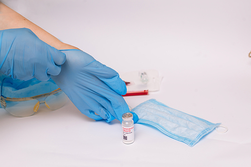 Coronavirus vaccine. Medical preparation in ampoule. Treatment for the disease, covid-19. The vaccine on a white background and on the background of a syringe, rubber gloves and goggles.