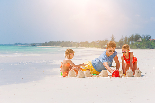 Father and two kids playing with sand on tropical beach