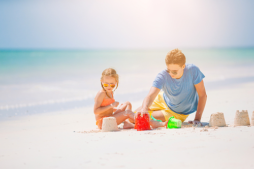 Father and little girl playing with sand on tropical beach making sand castle