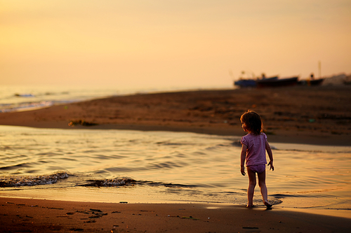 Little child having fun on a beach on sunset
