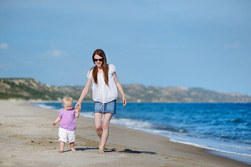 Mother and toddler daughter walking along a beach