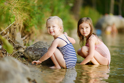 Two little sisters wearing swimsuits having fun in a river at summer