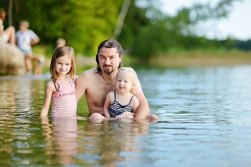 Two little sisters and their father having fun in a river at summer