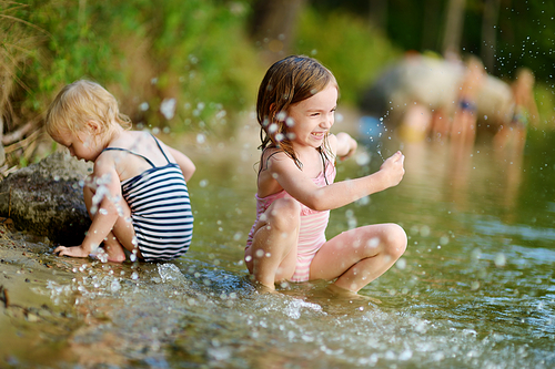 Two little sisters wearing swimsuits having fun in a river at summer