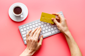 Shopping online with credit card. Keyboard, hands on pink desk top view.