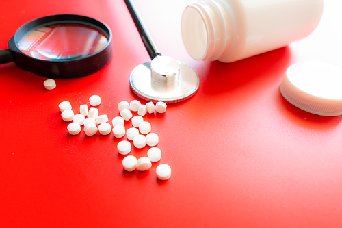 Magnifying glass, tablets and bottle on red reflection background. Checking ingredients and effectiveness of medicine.