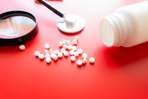 Magnifying glass, tablets and bottle on red reflection background. Checking ingredients and effectiveness of medicine.