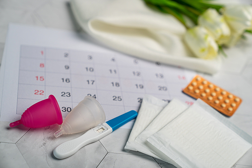 Pregnancy test, Birth control pill, menstrual cups and sanitary napkin pad with date of calendar background.