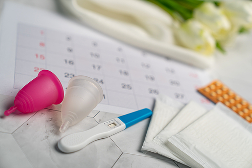Pregnancy test, Birth control pill, menstrual cups and sanitary napkin pad with date of calendar background.