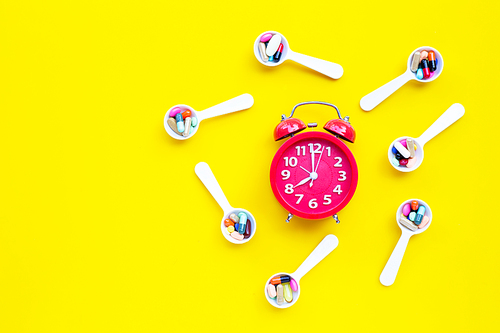 Clock with colorful tablets with capsules and pills on yellow background.