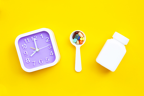 Clock with colorful tablets with capsules and pills on yellow background.