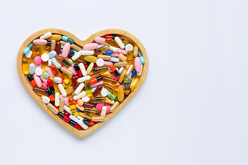 Colorful tablets with capsules and pills on white background. Wooden heart shape plate. Copy space