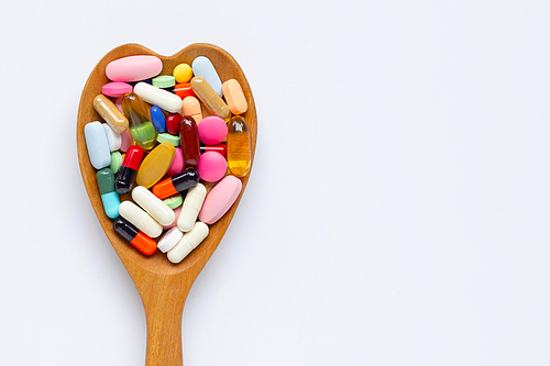 Colorful tablets with capsules and pills on white background. Wooden heart shape spoon. Copy space