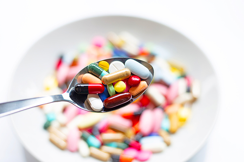 Various types of tablets, capsules and pills on  spoon with colorful medicine background. Top view