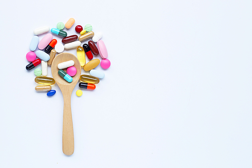 Colorful tablets, capsules and pills with wooden spoon on white background.