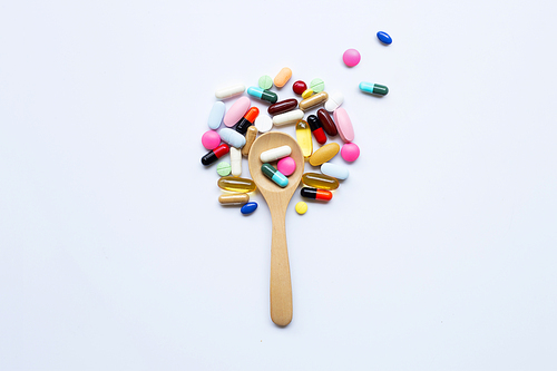 Colorful tablets, capsules and pills with wooden spoon on white background.