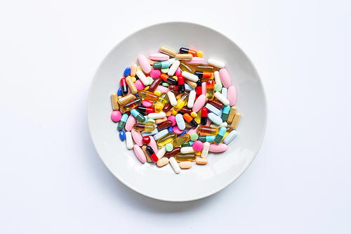 Colorful tablets with capsules and pills on white dish on white background.