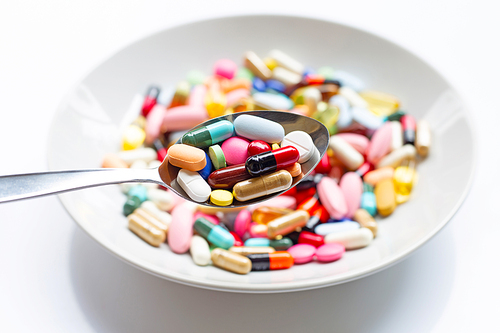 Various types of tablets, capsules and pills on spoon with colorful medicine background. Top view