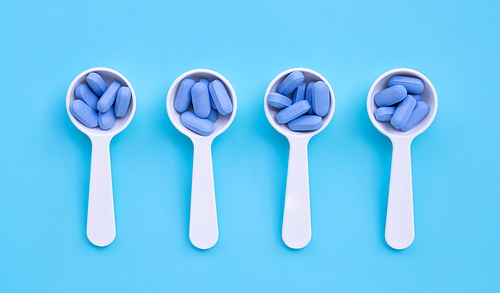 Medical blue pills with white plastic spoon on blue background. Top view