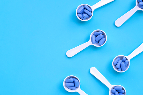 Medical blue pills with white plastic spoon on blue background. Top view