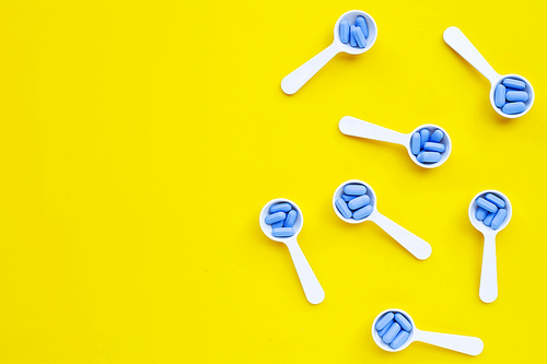 Medical blue pills with white plastic spoon on yellow background. Top view
