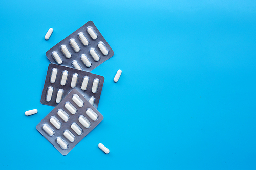 Capsule medicines in blister pack on blue background. Copy space