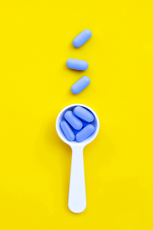 Medical blue pills with white plastic spoon on yellow background. Top view