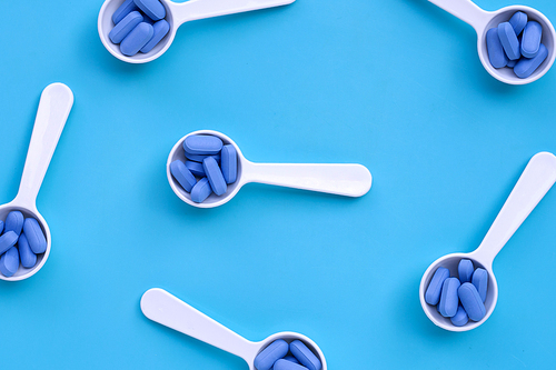 Medical blue pills with white plastic spoon on blue background. Top view
