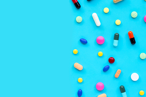 Colorful tablets with capsules and pills on blue background. Copy space