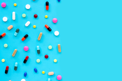 Colorful tablets with capsules and pills on blue background. Copy space
