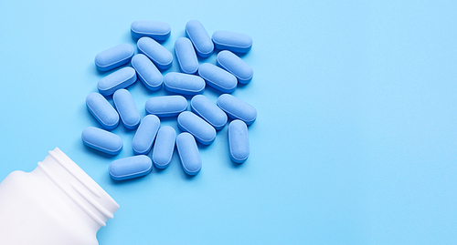 Medical blue pills with white plastic bottle on blue background. Copy space