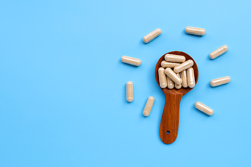 Herbal capsules with wooden spoon on blue background. Copy space