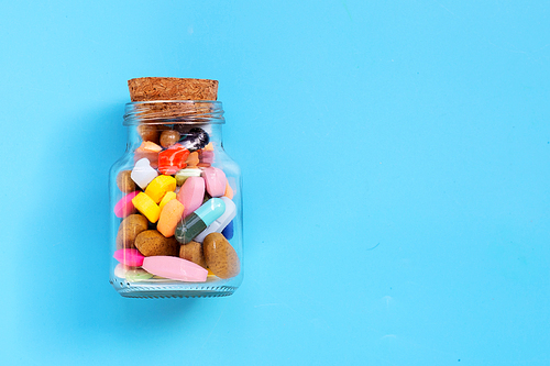 Colorful medicine pills, tablets and capsules in glass on blue background. Copy space