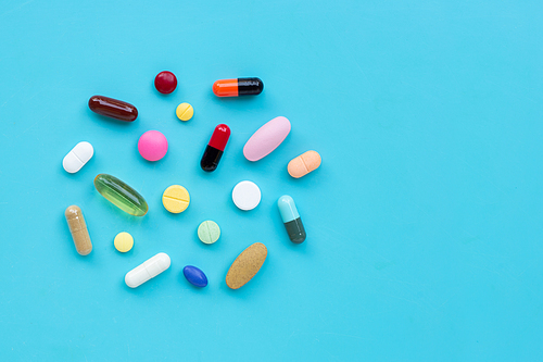 Colorful medicine pills, tablets and capsules on blue background. Copy space