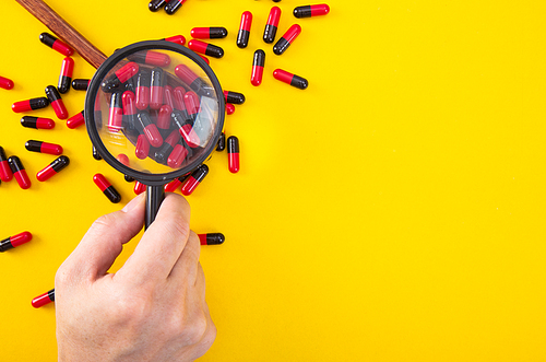 hand with a magnifying glass looking at pills. Medicine experimentl conceptual