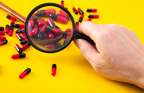 hand with a magnifying glass looking at pills. Medicine experimentl conceptual