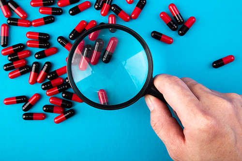 hand with a magnifying glass looking at pills. Medicine experimentl conceptual