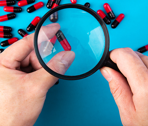 hand with a magnifying glass looking at pills. Medicine experimentl conceptual