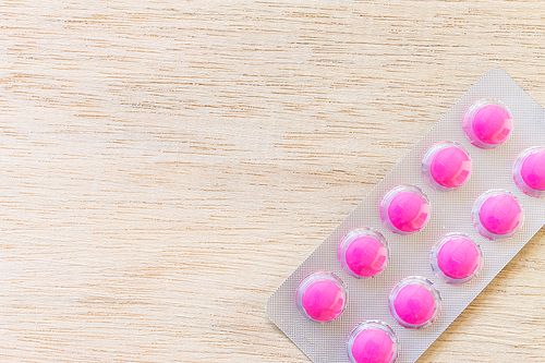 Pink pills in blister pack on wooden background