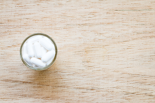 White pill in glass on wooden background