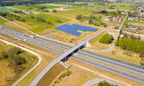 Aerial view to solar power plant near highway with traffic. Industrial background on renewable resources theme.