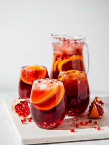 Winter sangria on white marble background. Jugful of sangria and glasses with orange slice and pomegranate. Copy space for text or design. Vertical.