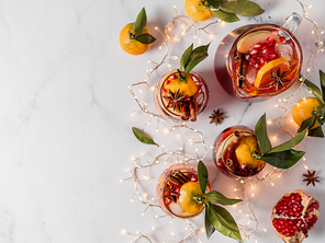 Winter sangria on white marble background. Jugful of sangria and glasses with with orange slice, pomegranate and spices. Copy space for text or design. Horizontal. Top view or flat lay.