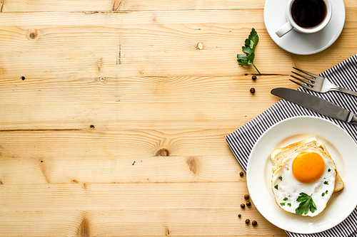 Fried eggs sandwich on plate - light wooden background top-down.